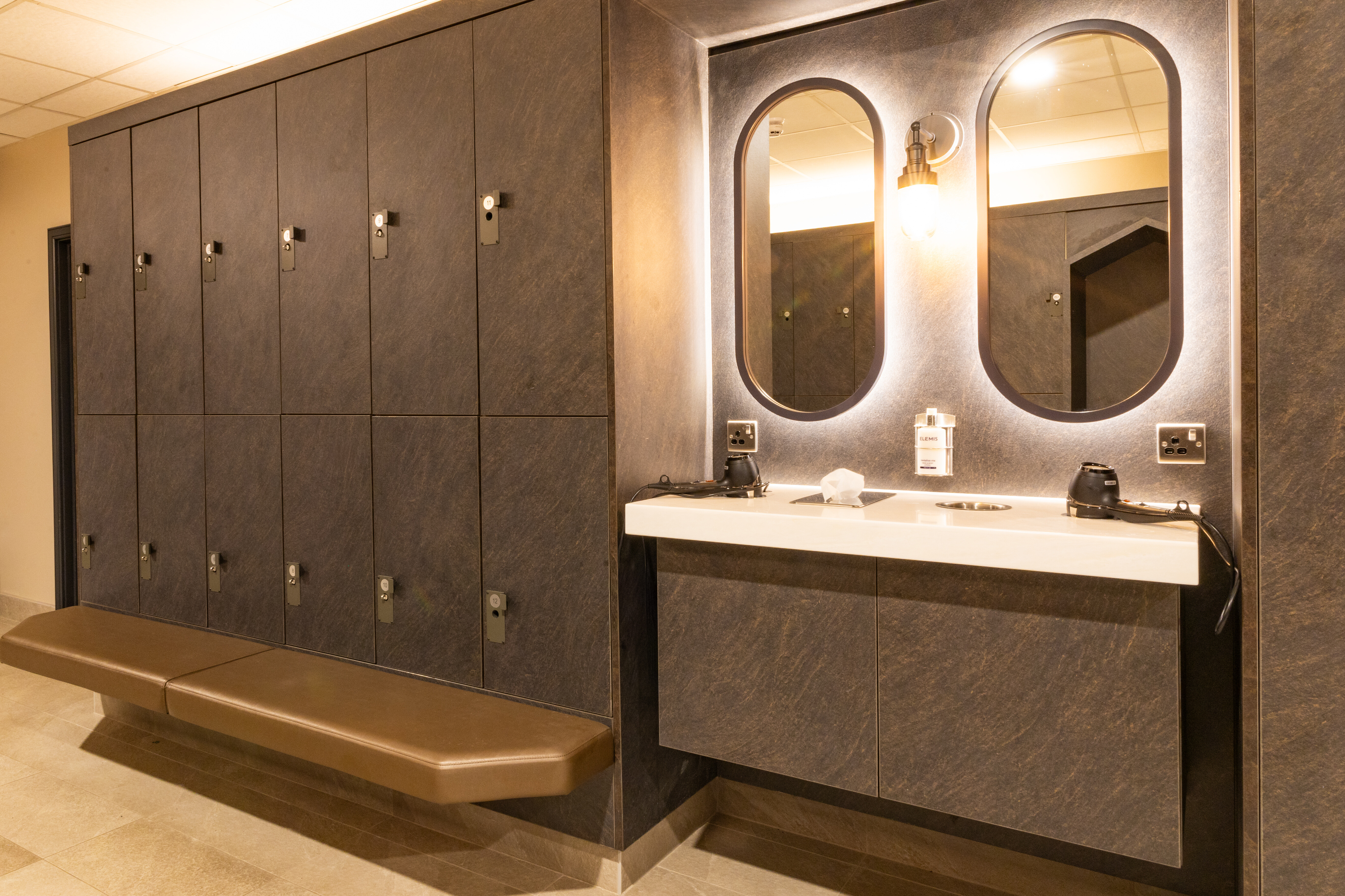 Mirrors with hairdryers next to lockers and a bench in the changing room