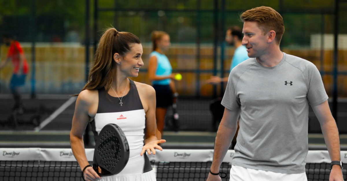 A couple playing doubles padel chat as they walk away from the net
