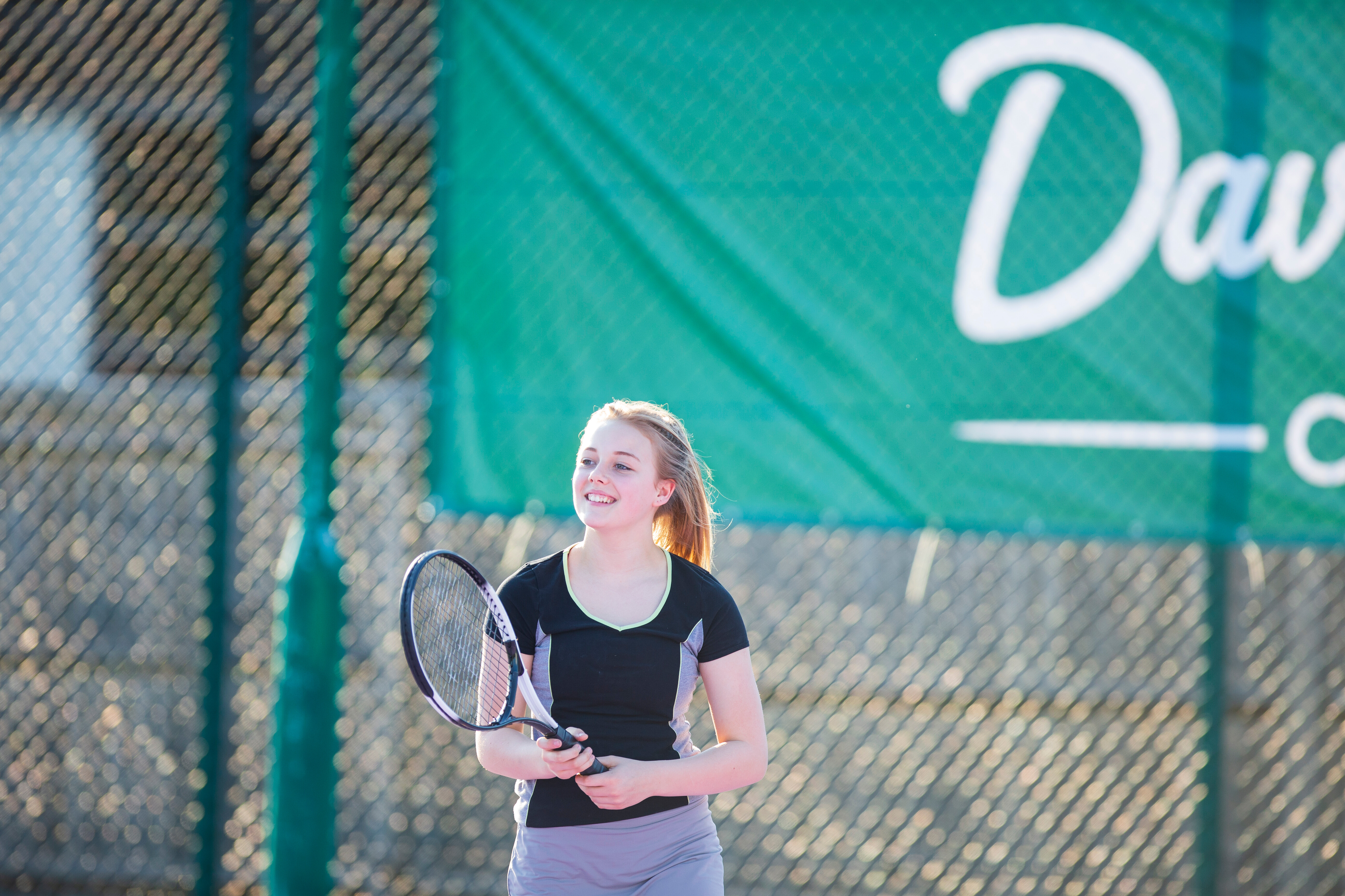 A teenager holding a tennis racquet in an outside court