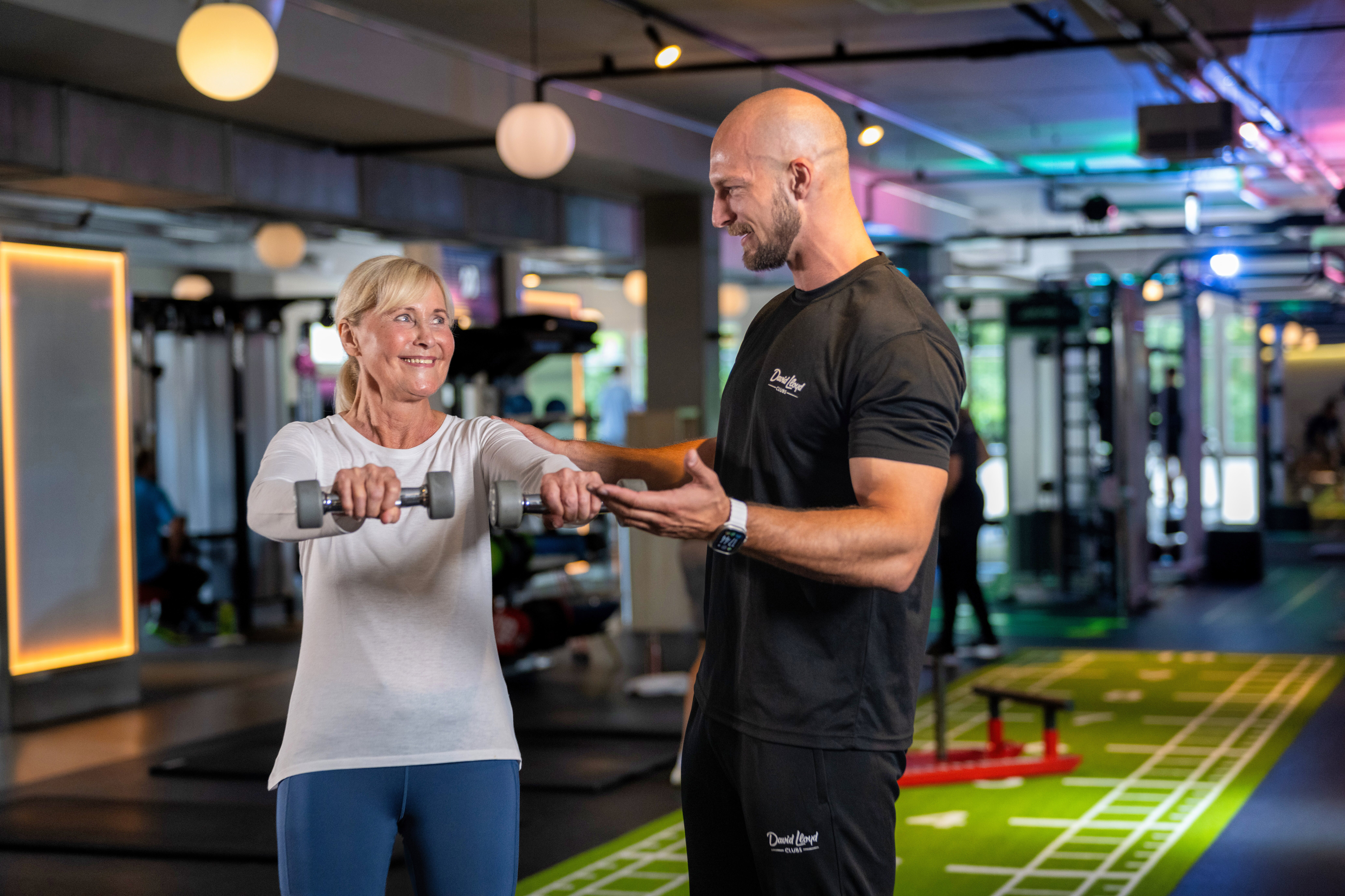 A woman lifts weights and her personal trainer looks proud of her achievement