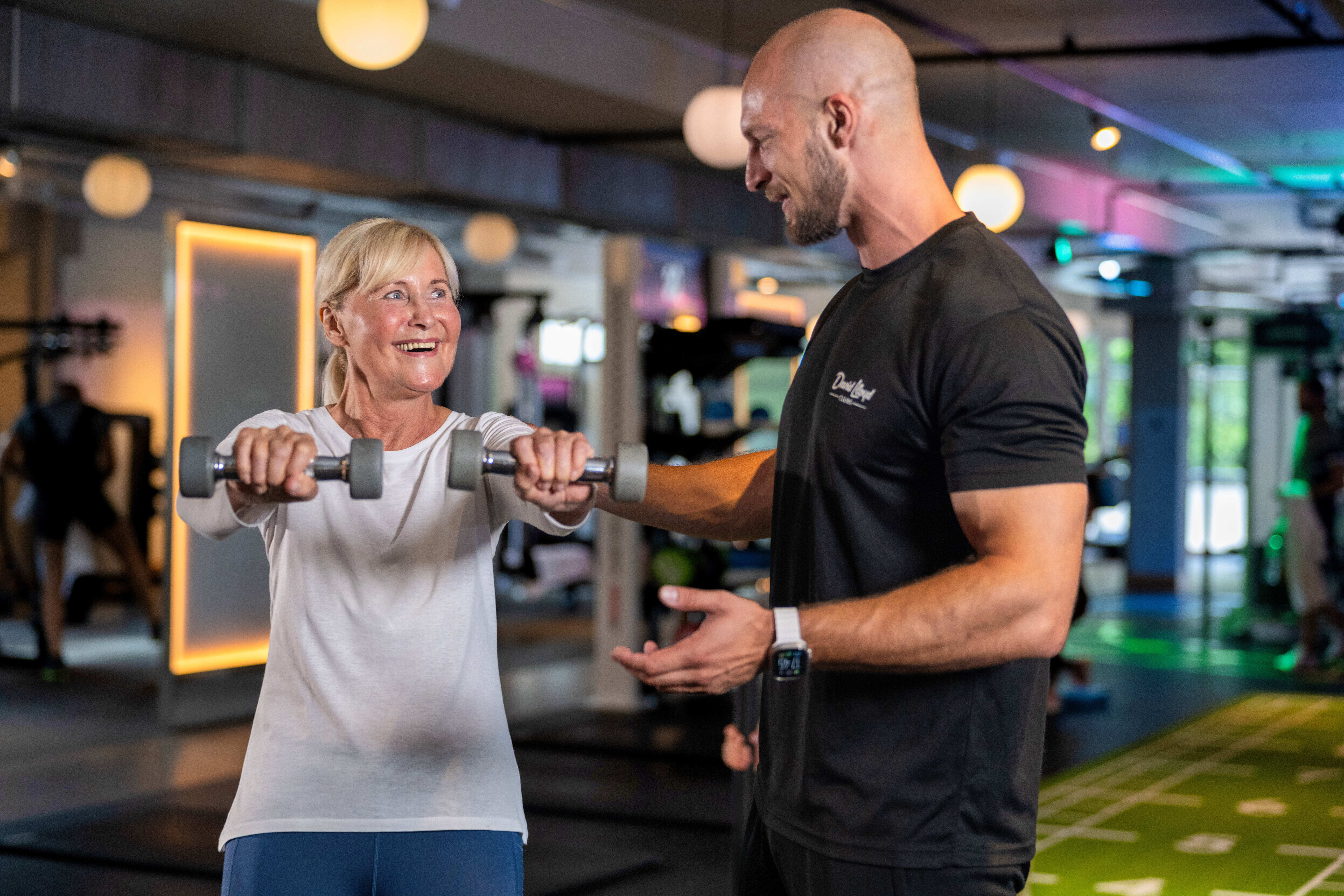 A woman smiles while lifting weights as her personal trainer watches