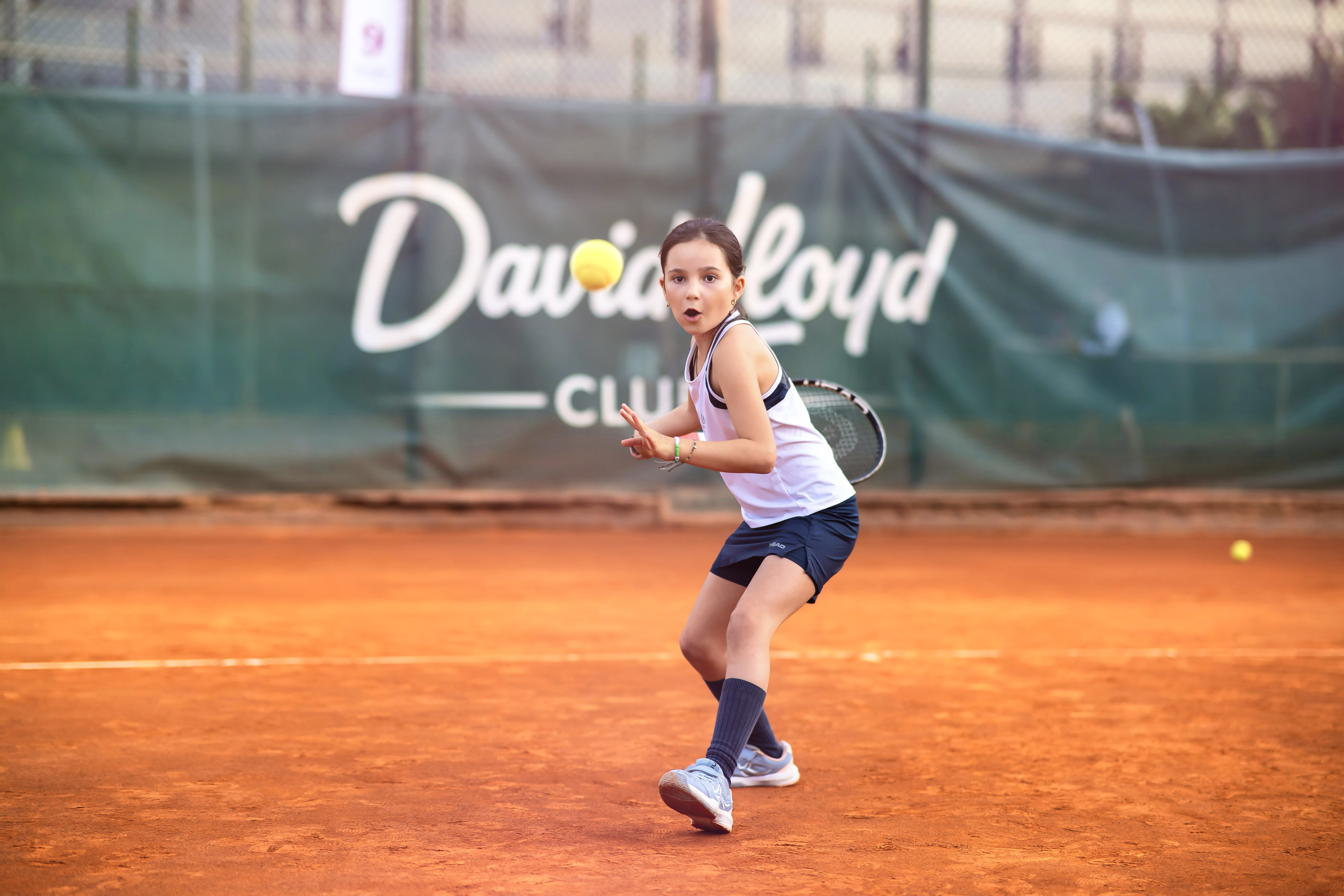 A girl playing tennis on an outdoor clay court is about to hit the ball