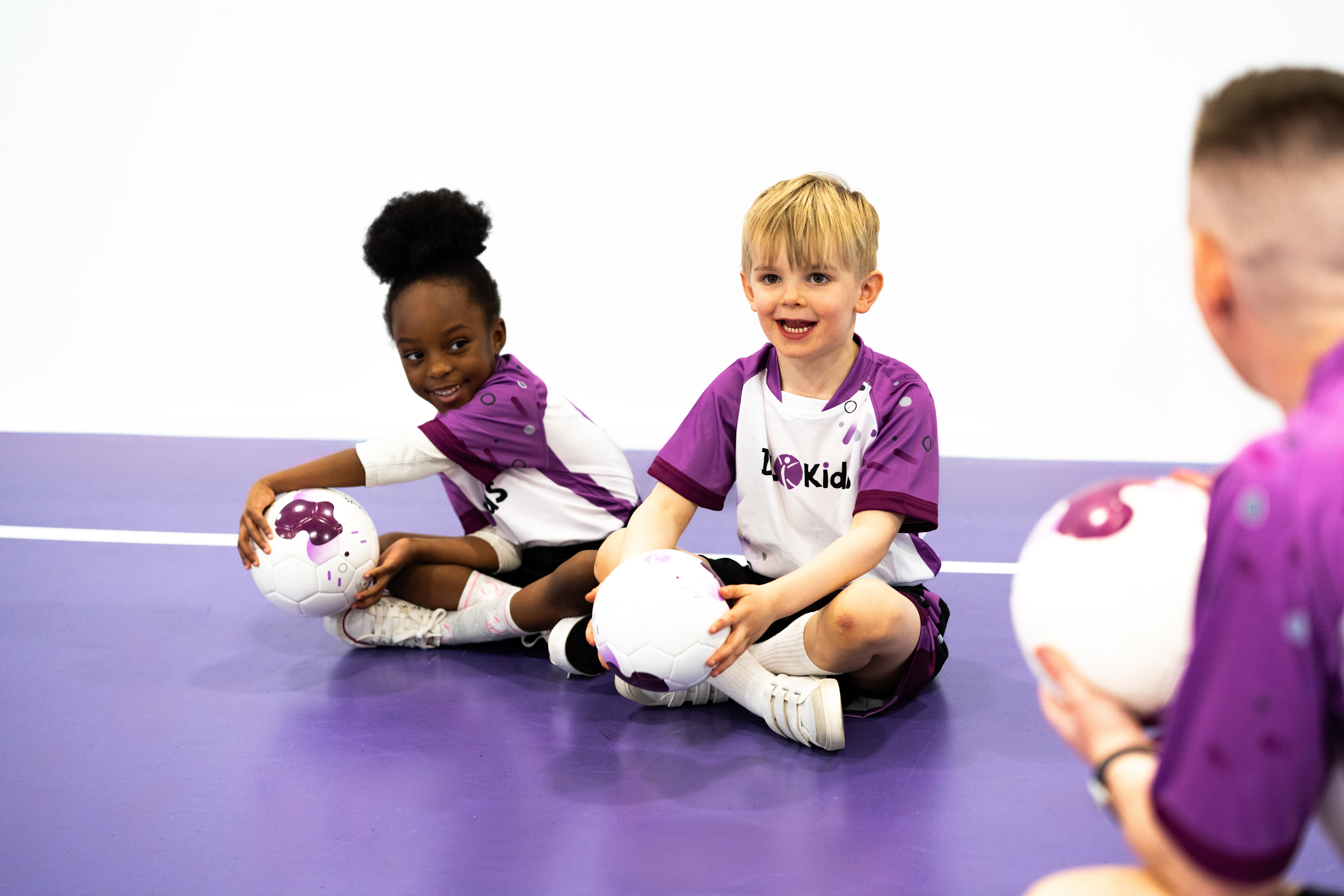 A group of young children holding footballs and listening to their instructor