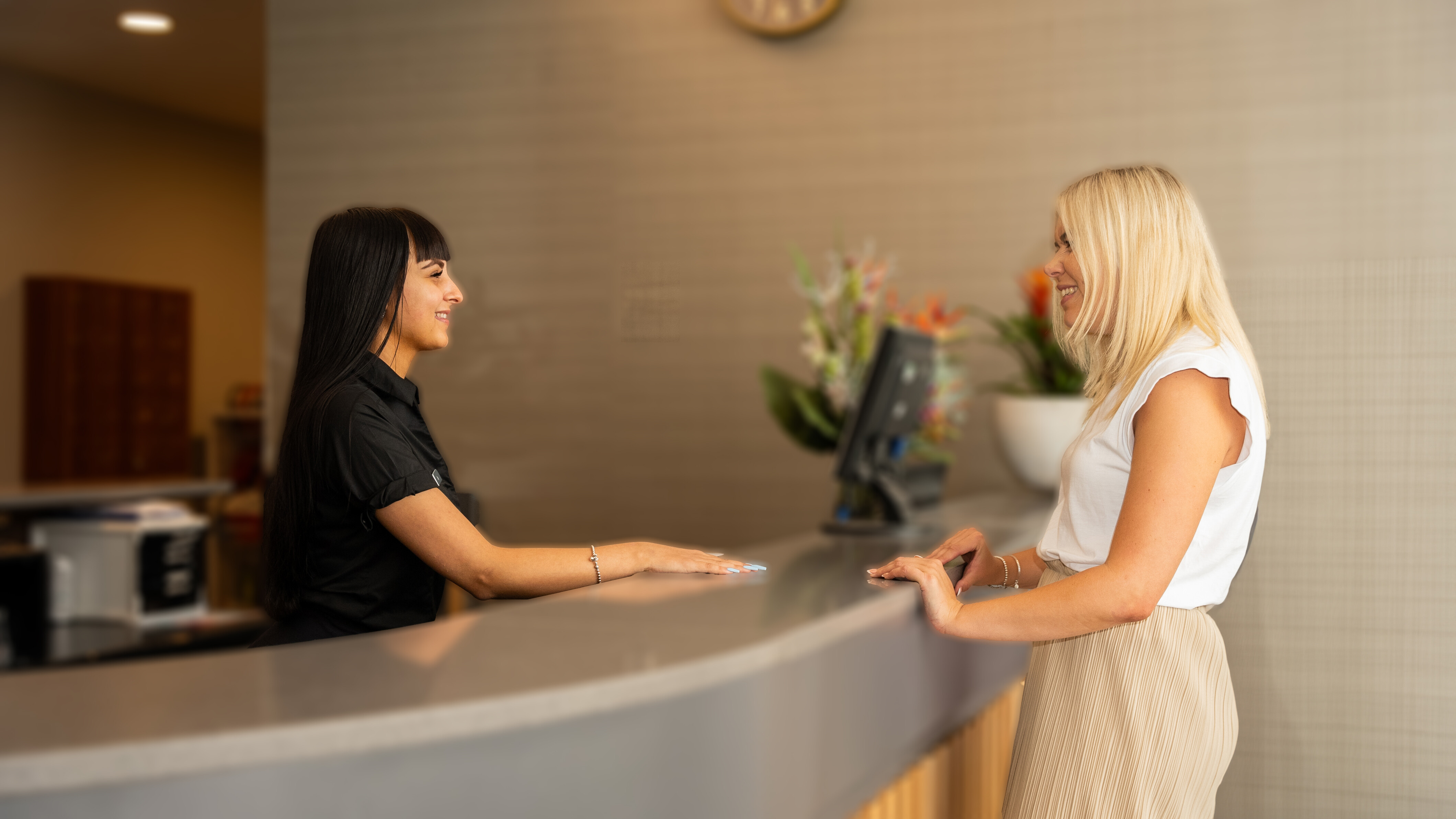A receptionist greets a smiling woman, welcoming her to David Lloyd