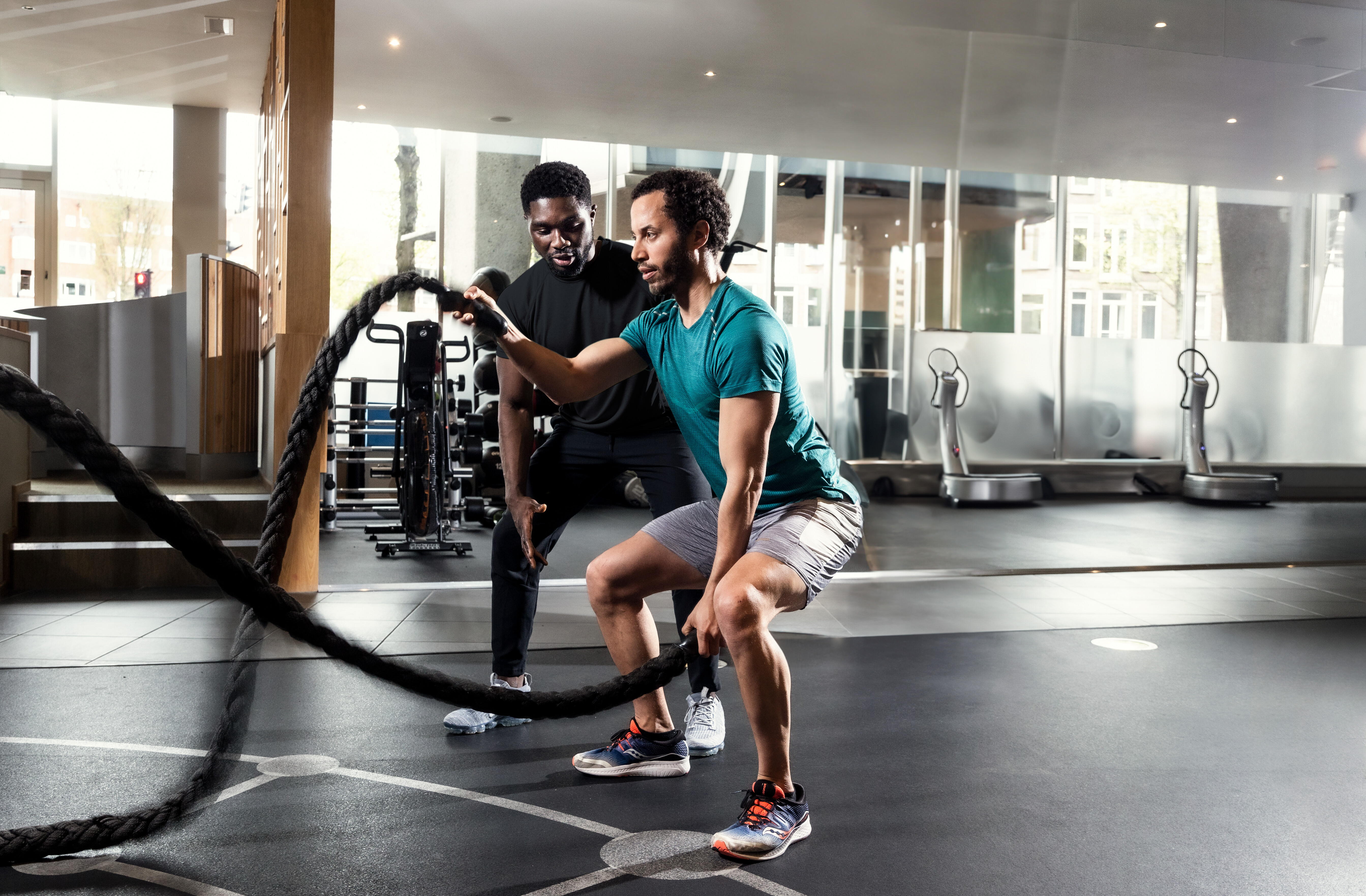 A personal trainer encourages a man using the battleropes