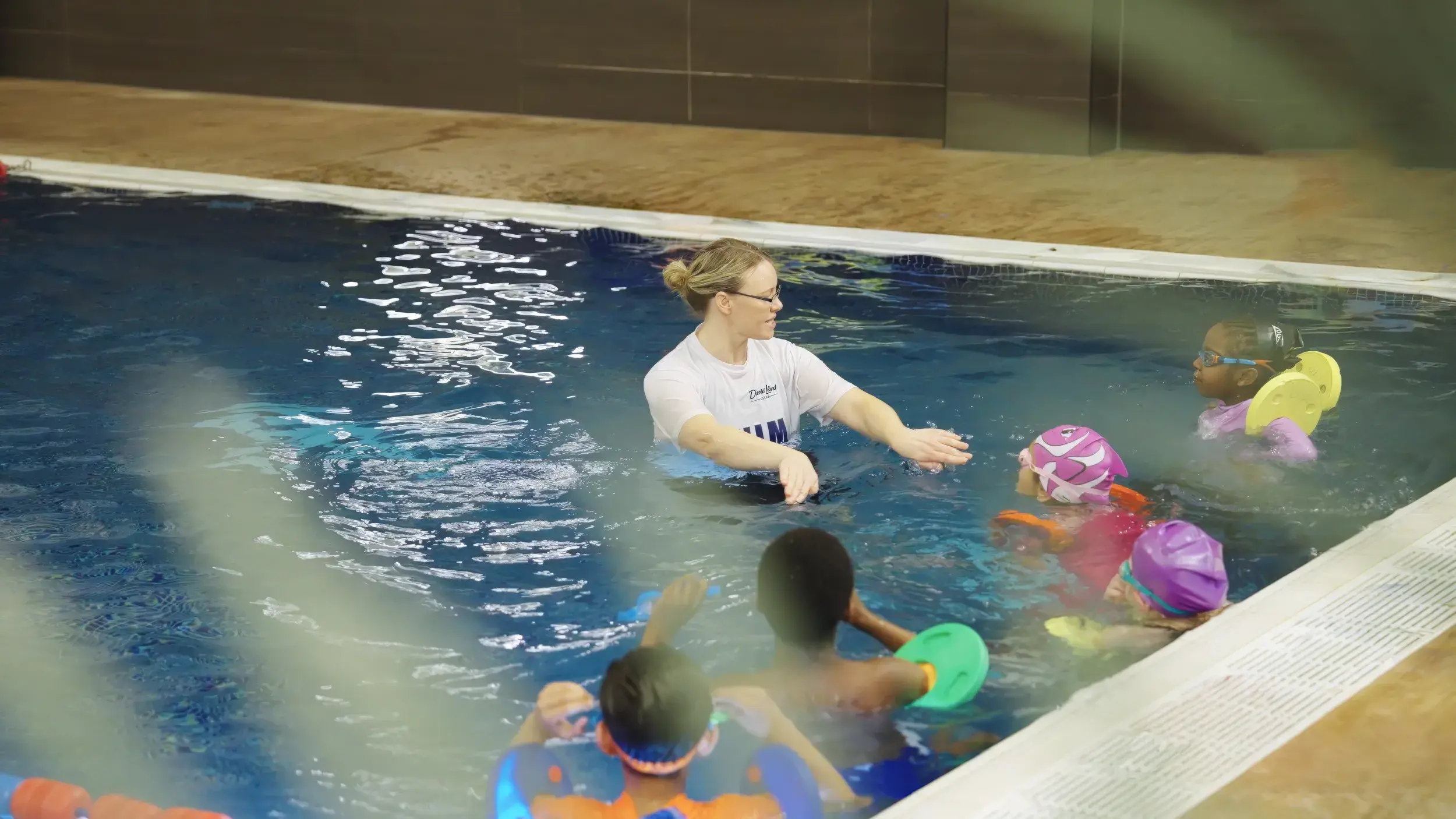 A group of children in an indoor pool with a swimming instructor