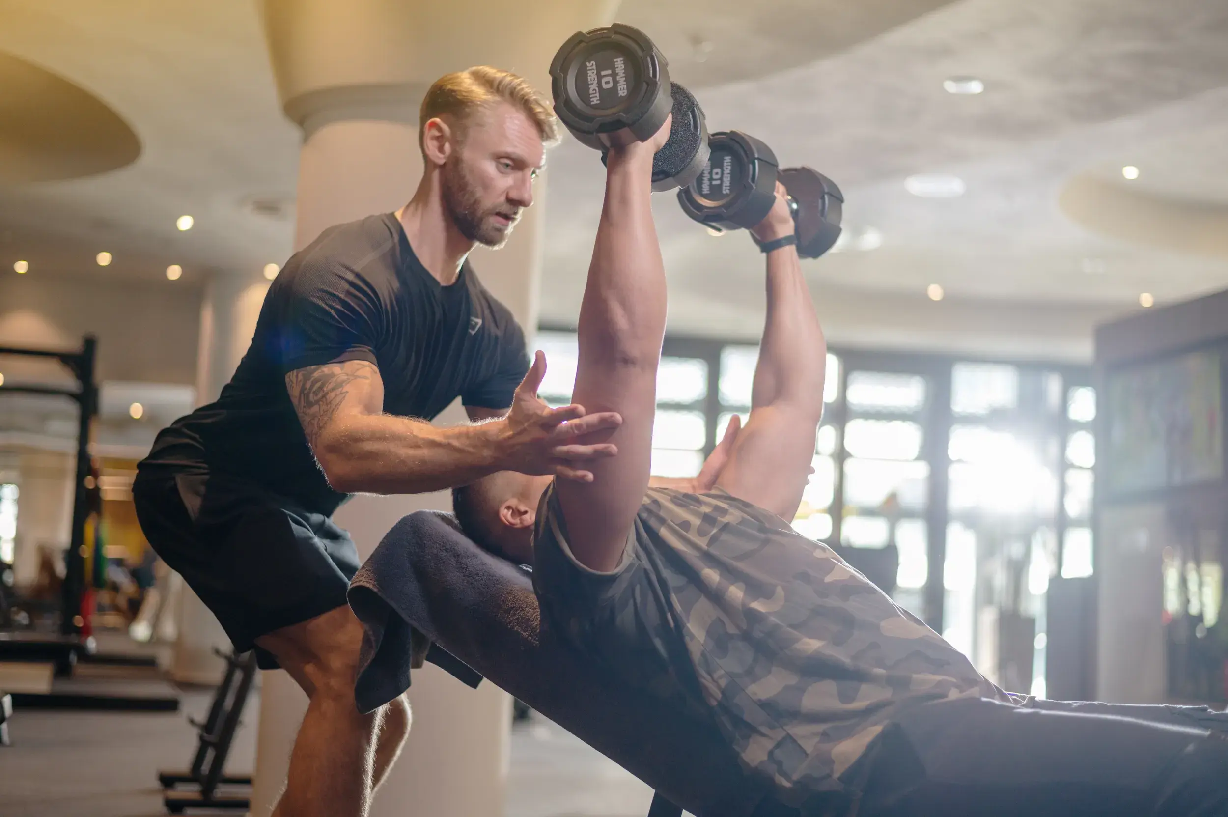 A man lifting weights while his personal trainer supports him