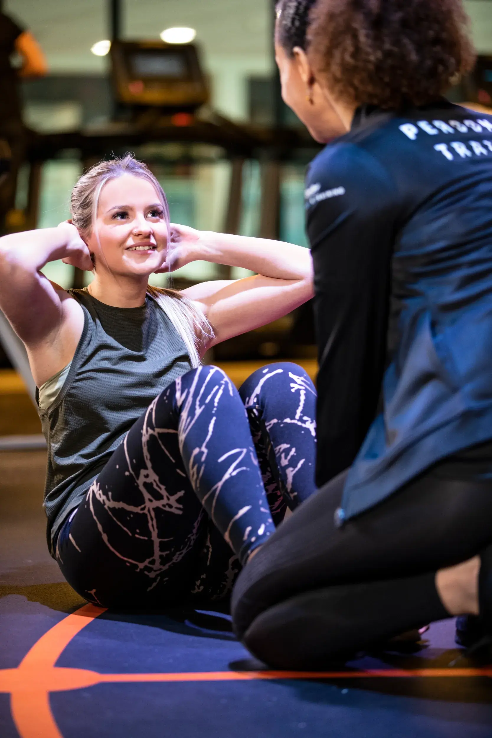 A young woman smiling while doing sit ups with her personal trainer holding her feet