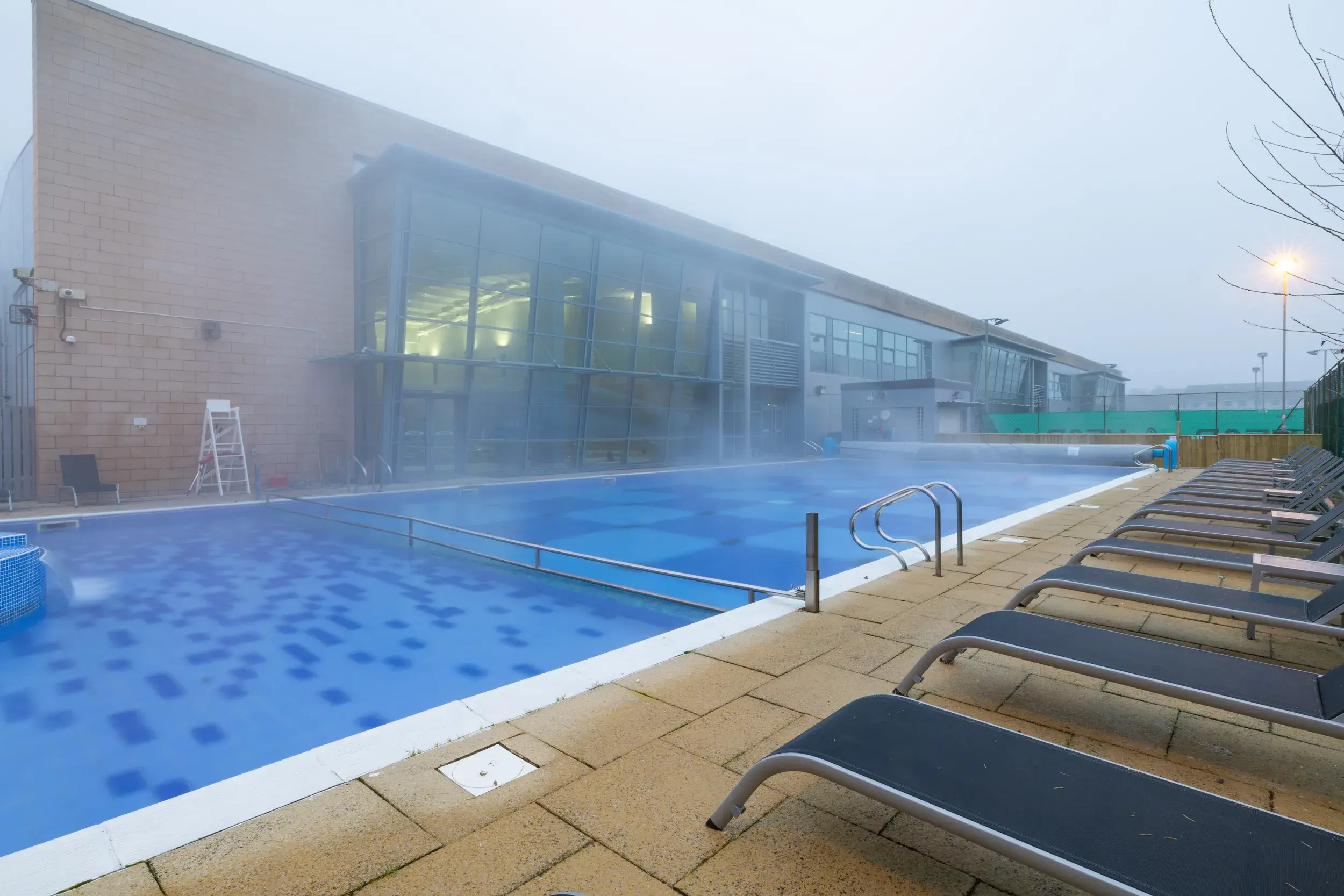 The outdoor pool at David Lloyd Glasgow West End. Steam rises from the pool, which has loungers on the poolside
