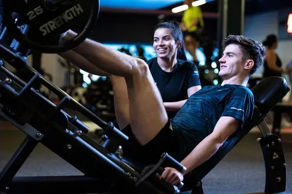 A man pushing a weight with his legs, working with a personal trainer