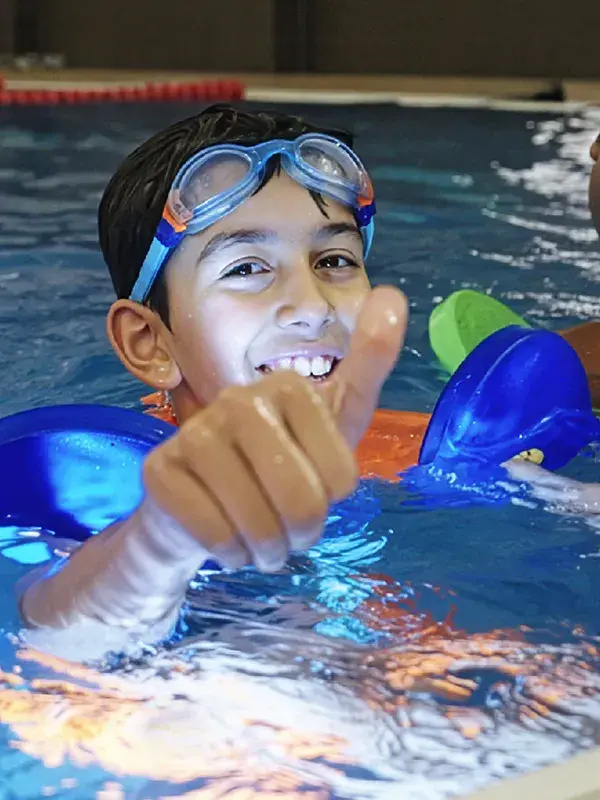 Two boys in the swimming pool, one with his thumbs up