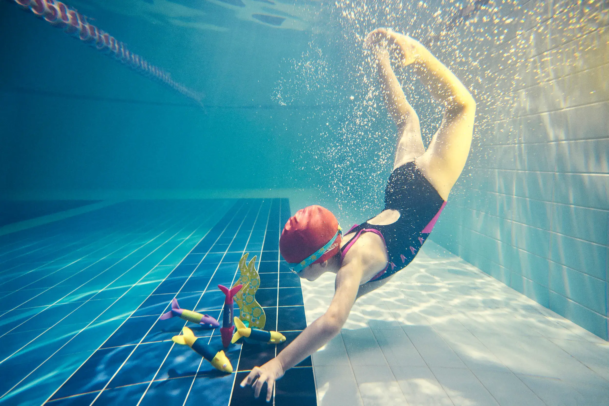 A young girl retrieving some dive sticks from the bottom of the swimming pool