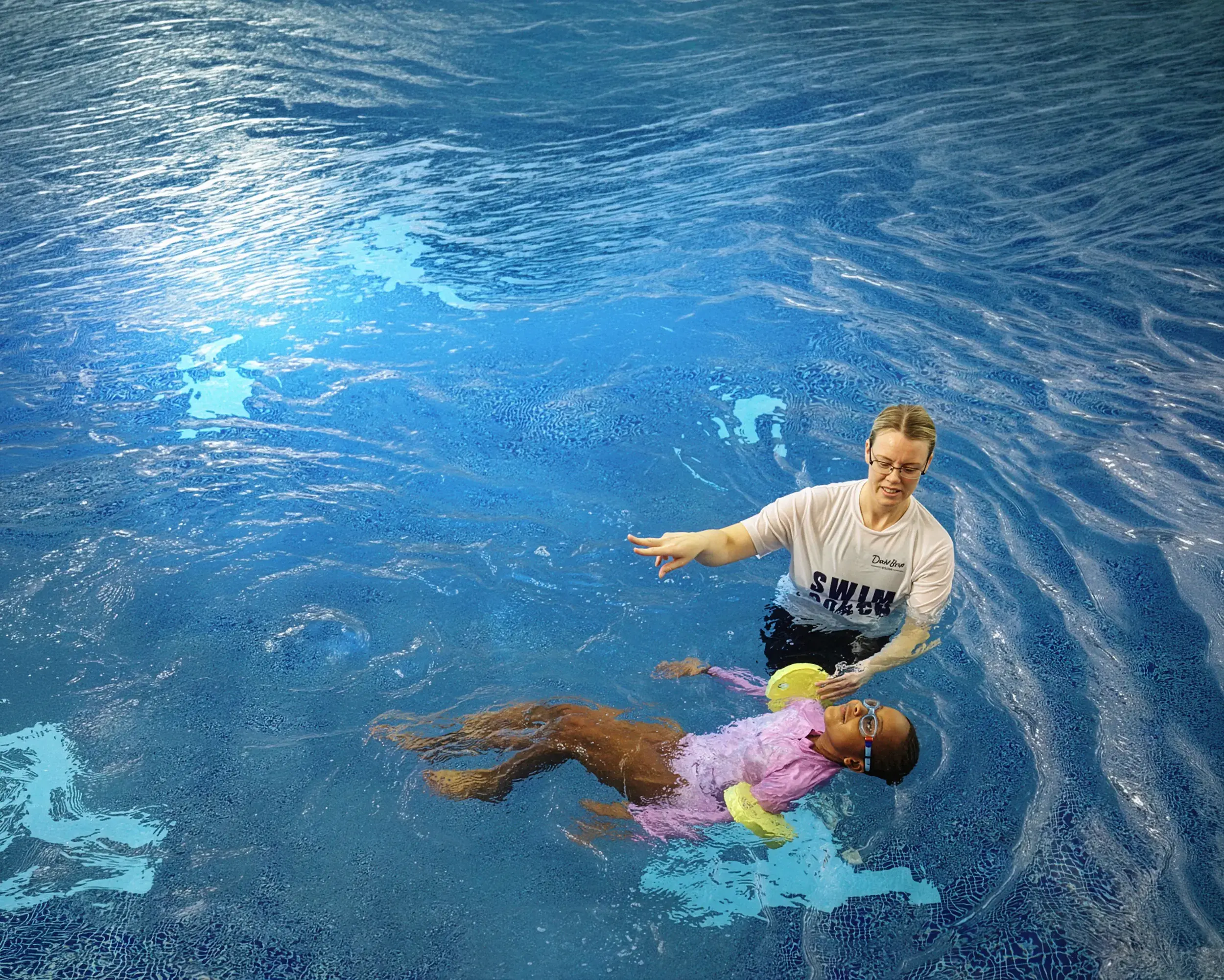 A swimming coach in a pool with a girl learning to swim