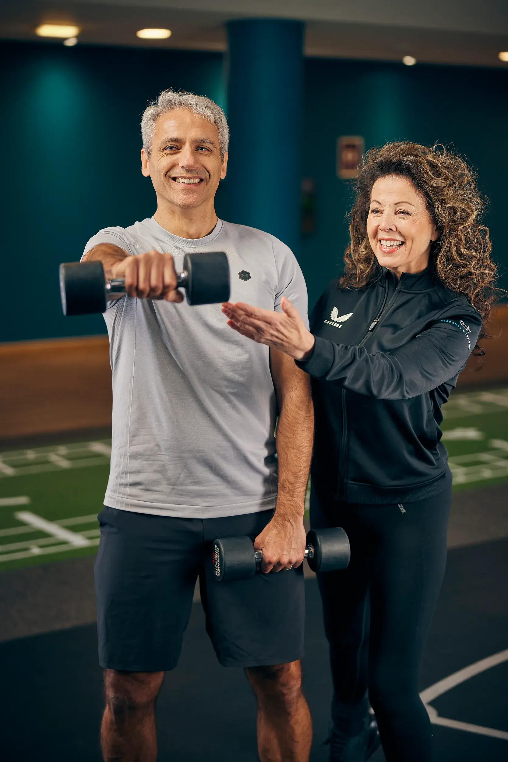 A man holds a weight as his personal trainer smiles at his progress