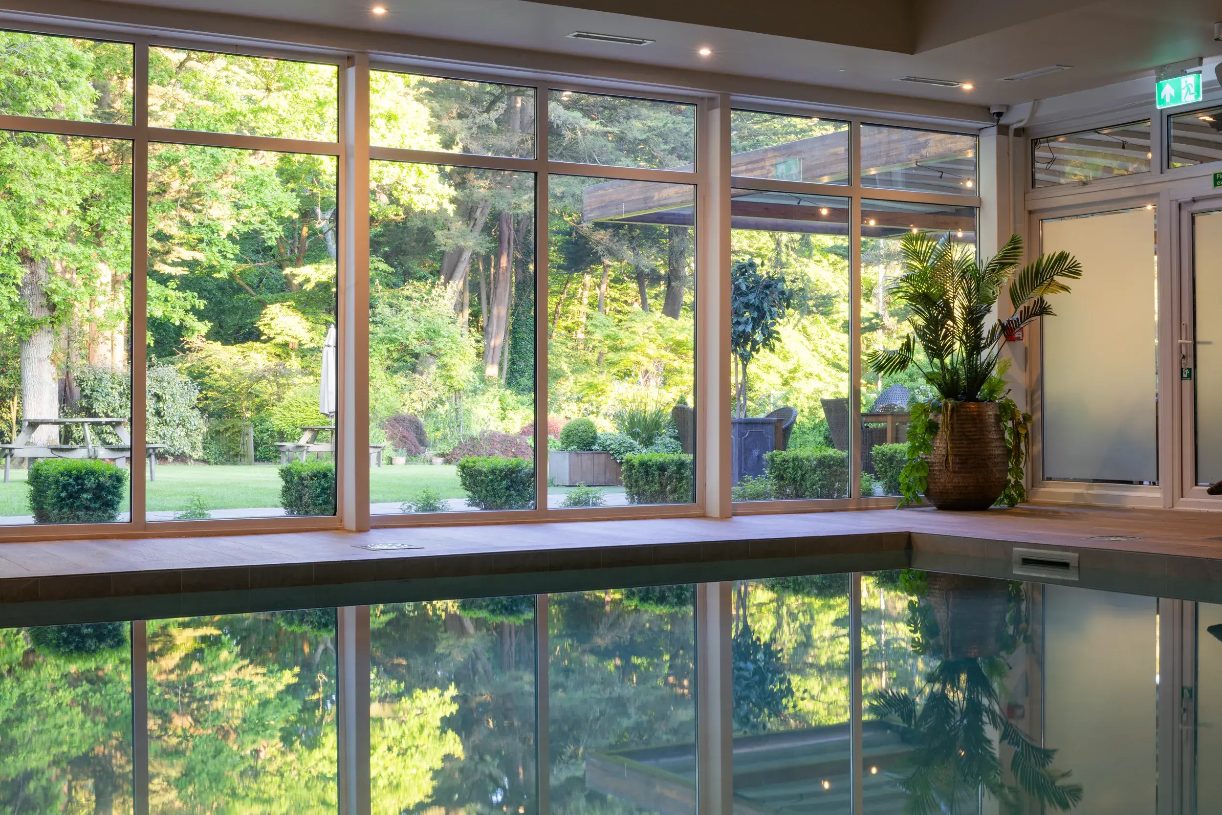 The indoor swimming pool with large windows to woodland outside, with is reflected on the surface of the water